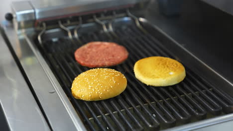 two buns are grilled on a barbeque grid. raw cutlet being fried on grill. unhealthy tasty dish.