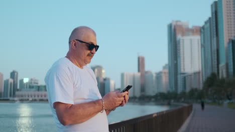 Bearded-senior-man-standing-outdoors-using-smartphone.-Retired-male-reading-news-chatting-with-his-children-via-mobile-phone.-Studying-city-map-app.-Lost-in-city-looking-for-right-direction.