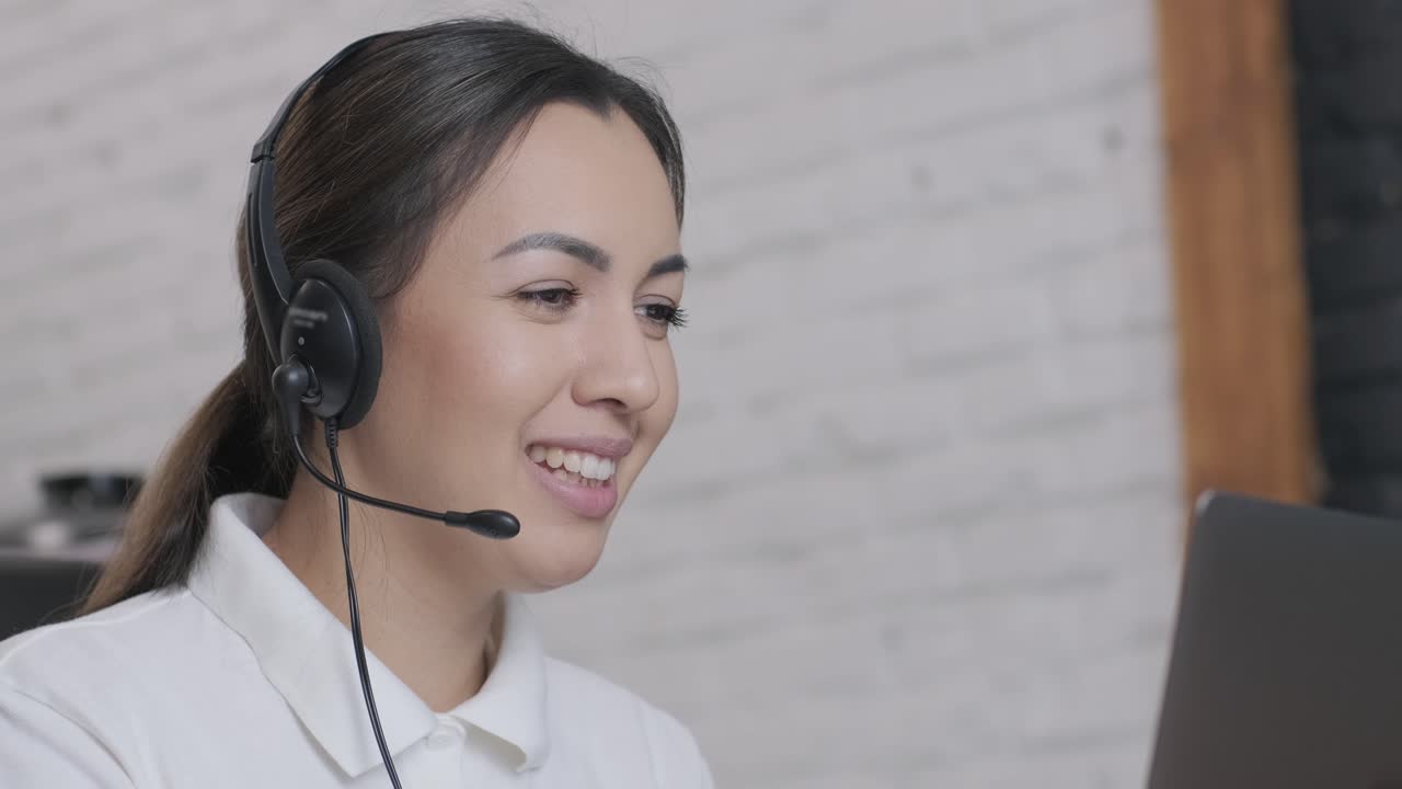 Smiling woman call centre operator, customer support agent wears headset consults client online typing on laptop, talk in internet computer chat, helpline operator secretary make conference video call