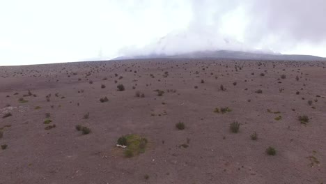 Drone-Volando-Sobre-Una-Llanura-Desértica-Con-Un-Volcán-Humeante-En-La-Distancia