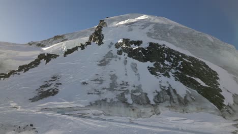 aerial-tilt-down,-rocky-summit-covered-with-snow-and-ice-in-the-swiss-alps