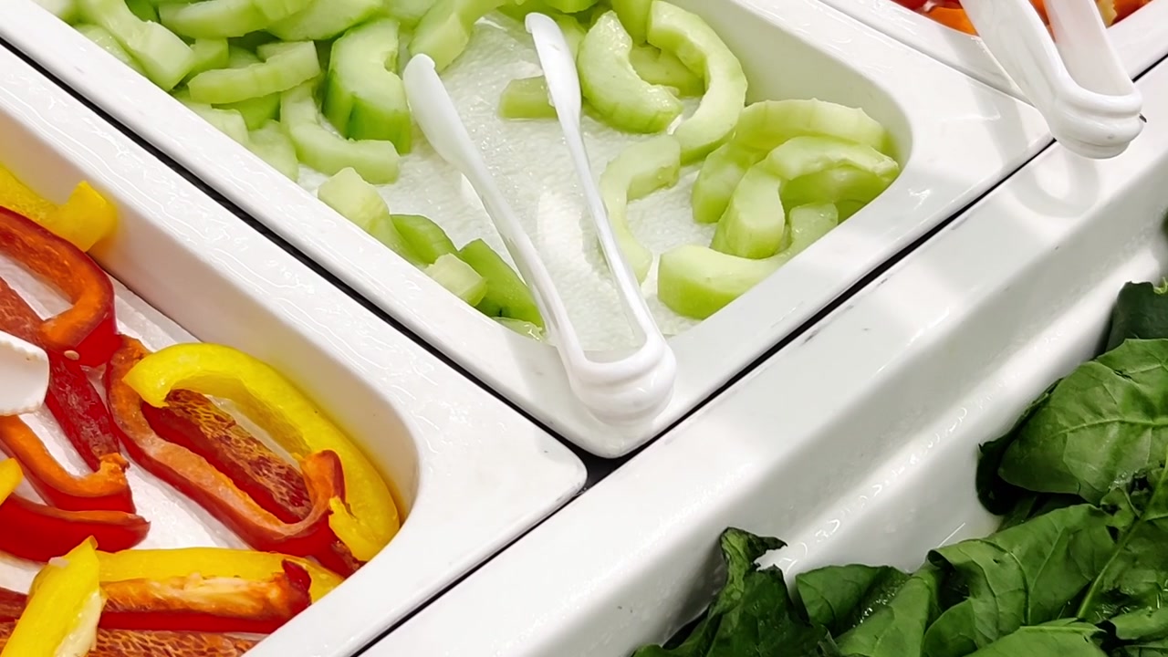 Variety buffet of vegetable food arranged on white trays with tongs