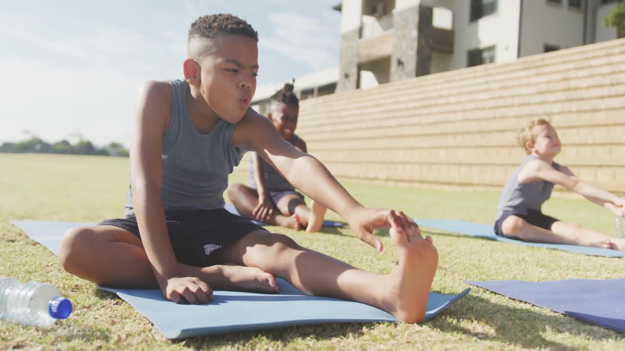 video de niños diversos enfocados practicando yoga en esteras en un día soleado