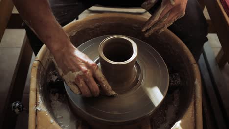manos de un joven alfarero trabajando en la rueda de un alfarero y haciendo una olla