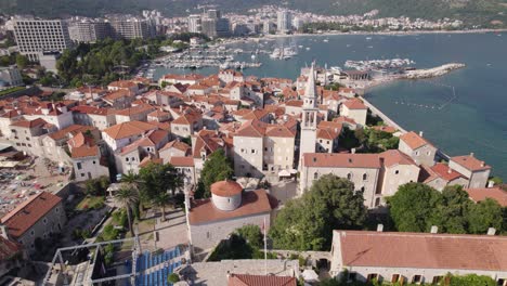 aerial orbiting shot of old budva town with marina and coastline as background, montenegro