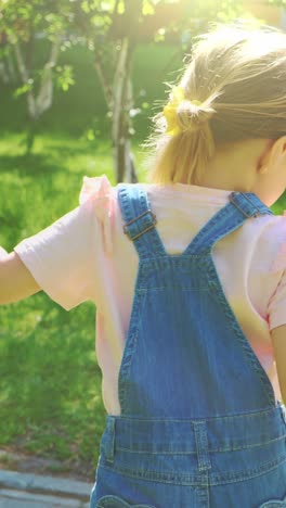 young girl in denim overalls walking in a sunlit garden with vibrant greenery and playful atmosphere