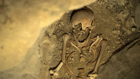 human skull and bones in dirt archeology discovery in cave, panning shot