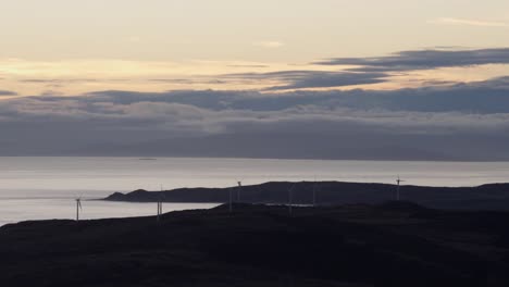 Hermoso-Paisaje-De-Nueva-Zelanda-Con-Océano-Y-Montaña-Distante-Durante-La-Puesta-De-Sol-Con-Molinos-De-Viento