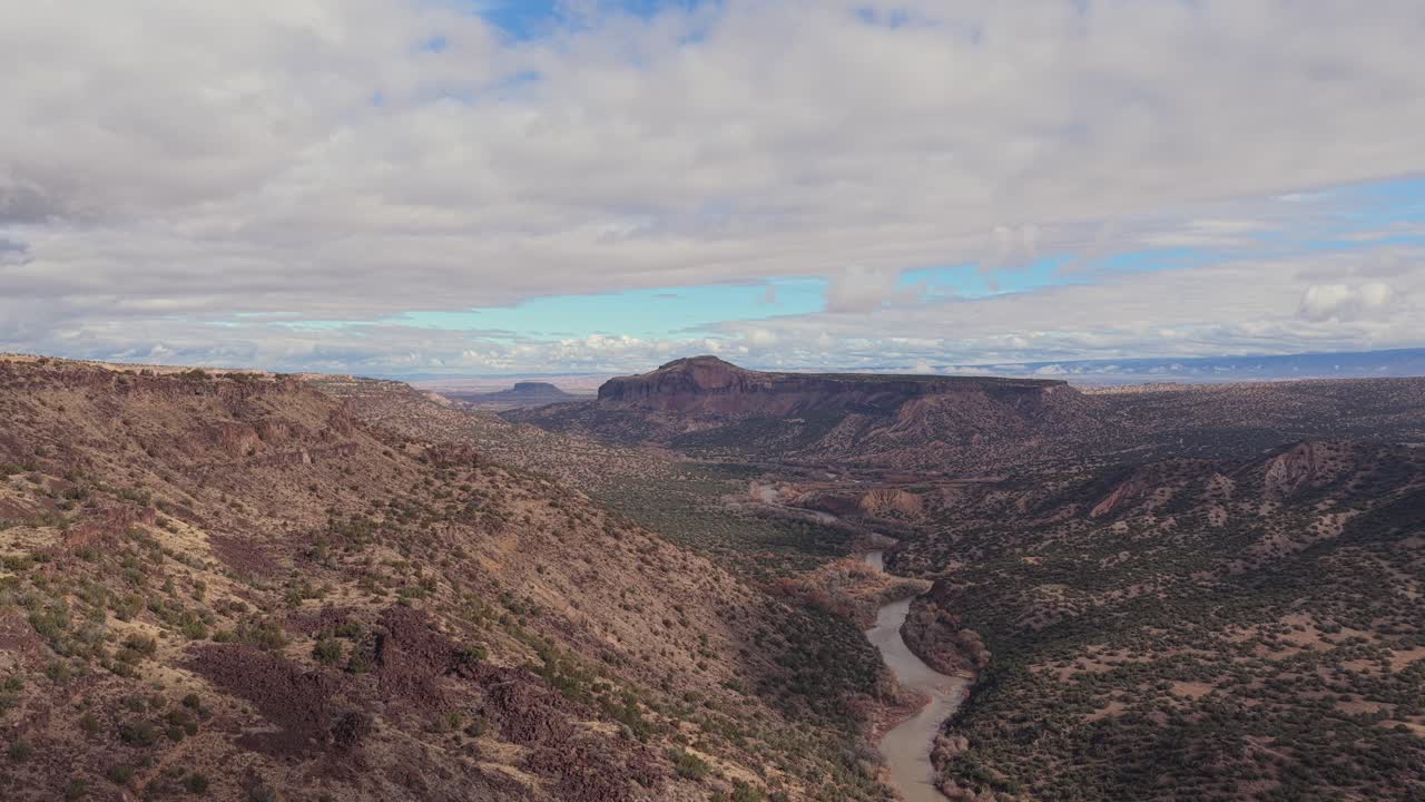 A smooth lateral move along the canyon rim reveals the Rio Grande winding through rugged desert terrain beneath scattered clouds