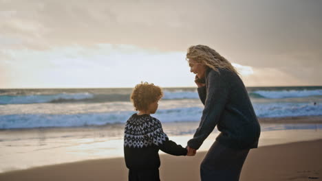 Madre-E-Hijo-Descansando-Juntos-En-La-Orilla-Del-Atardecer-De-Otoño.-Mujer-Sonriente-Hablando-Por-Teléfono