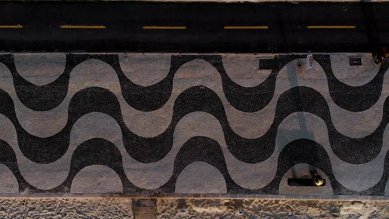 panorámica aérea lateral temprano en la mañana que muestra los patrones en el pavimento de la acera, el carril para bicicletas y la playa de copacabana