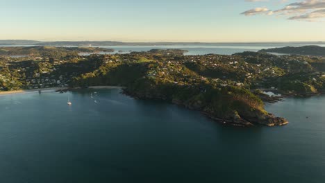 Waiheke Island, coastline at sunset, calm bay with sailboats, golden light. New Zealand. Aerial drone panoramic view, landscape. Copy space