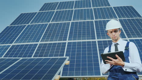 a young businessman in a white helmet uses a tablet on the background of solar panels alternative en