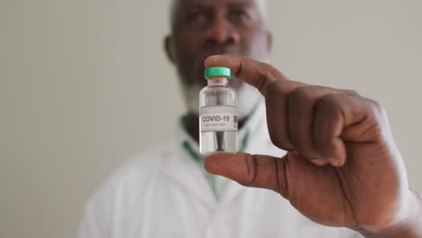 close up of male african american doctor holding vaccine bottle at hospital