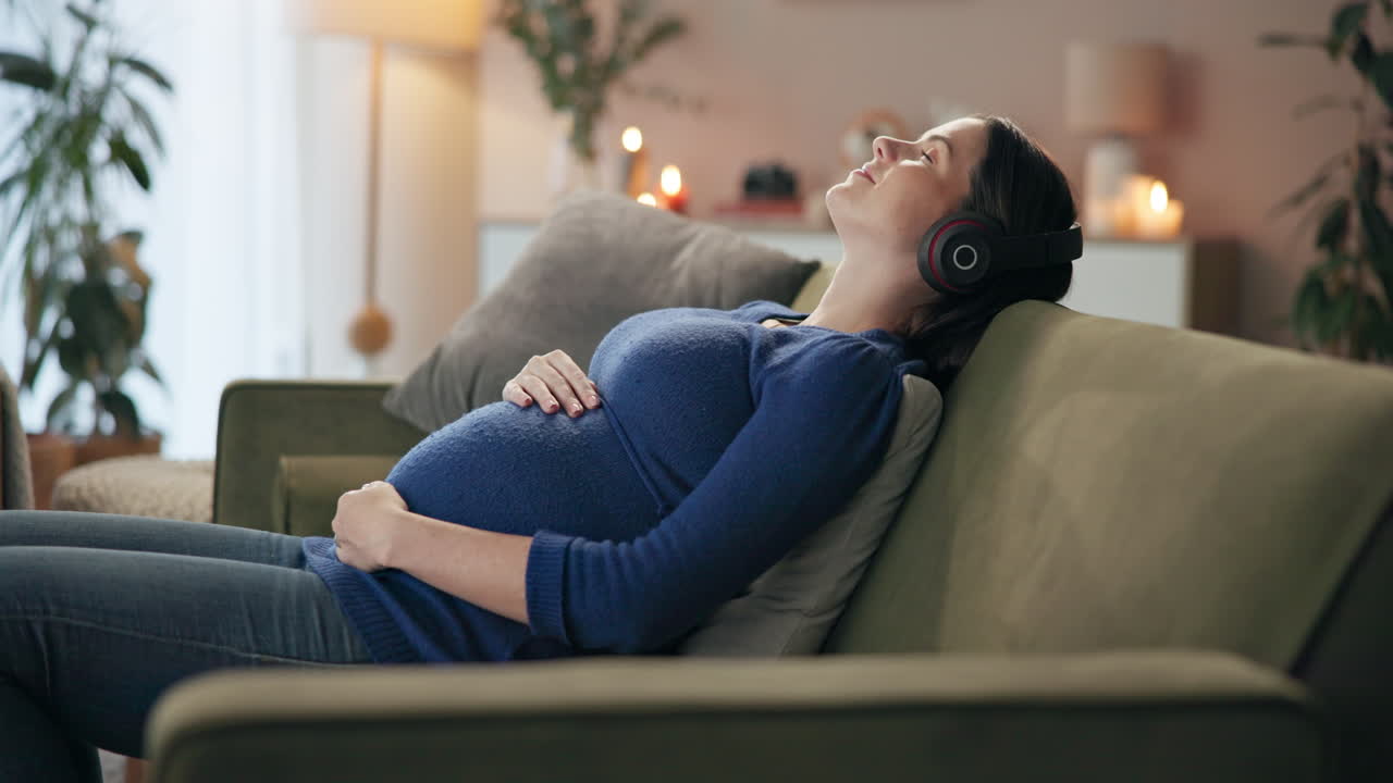 Pregnant woman relaxing on couch with headphones