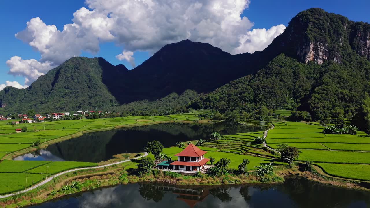 Aerial video capturing lush green rice fields and a serene lake with a traditional house, set