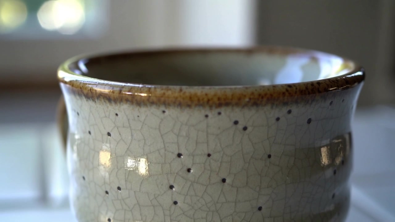 Camera pulling back revealing brown rim crackle cup specked on counter by window, revealing handle