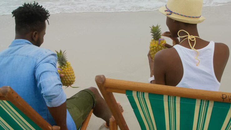 Coppia afroamericana di spalle che beve succo d'ananas sulla spiaggia 4K
