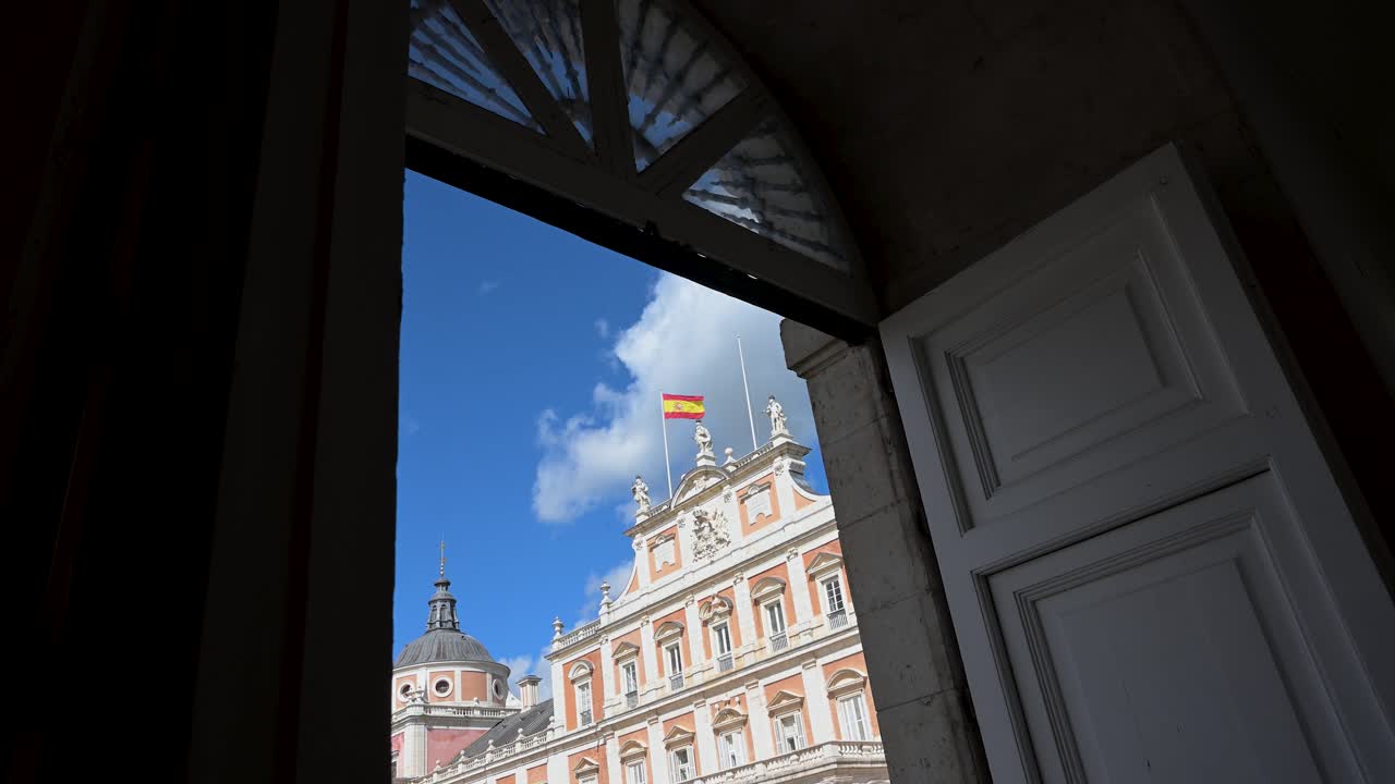 Framed by a doorway on a sunny day, Spain's Aranjuez Royal Palace reveals its 18th-century grandeur; its celebrated architecture a key tourist landmark of rich royal heritage.
