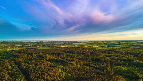 an aerial hyperlapse captures a sweeping forward motion over a diverse latvian landscape of lush green forests and patchwork fields under a dynamic sky with fast-moving clouds at sunset