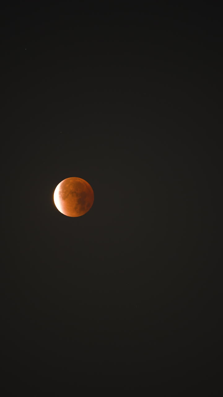 Vertical timelapse of a lunar eclipse showing a red blood moon phase against a dark night sky. Minimal composition, ideal for mobile, social media, and vertical formats