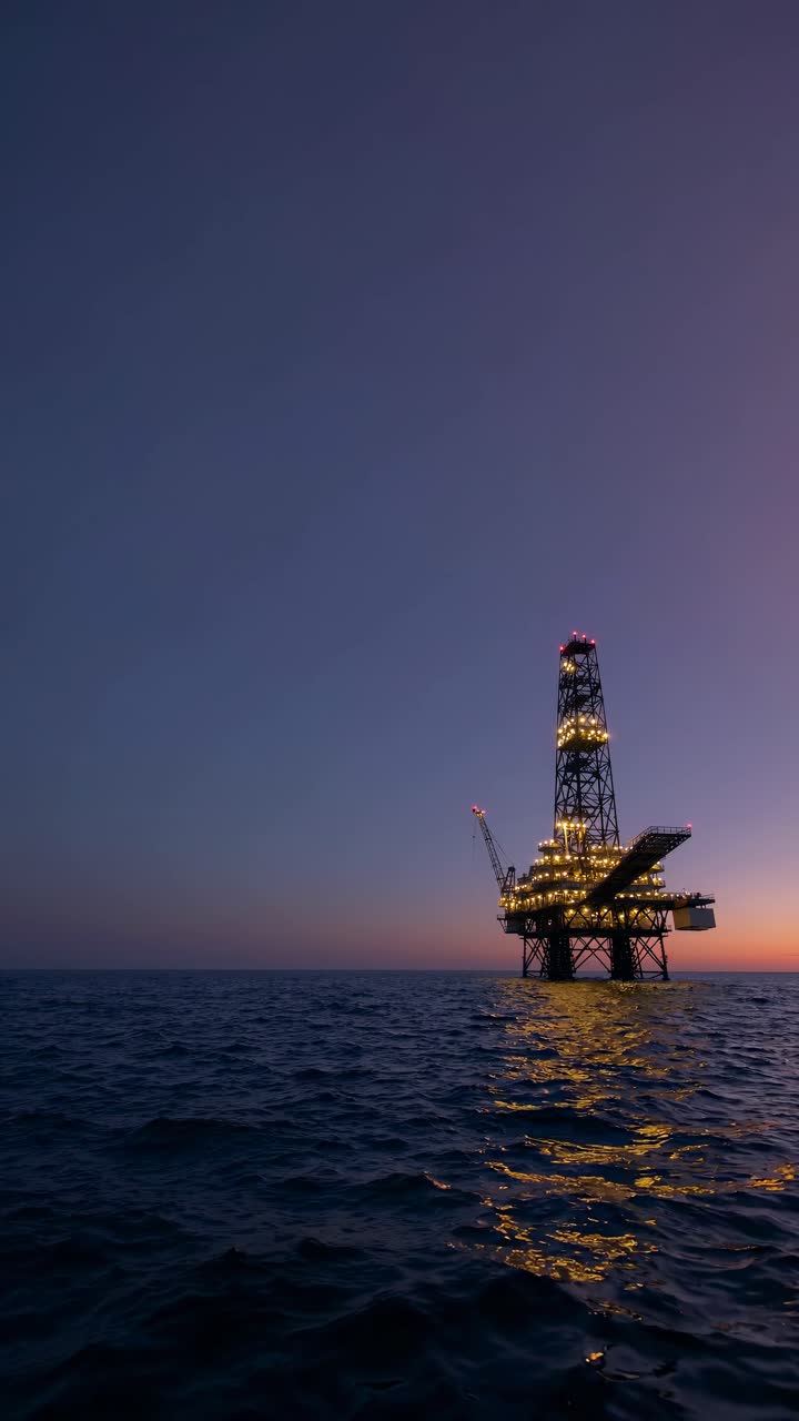 Industriel offshore olieboreplatform oplyst i skumringen på havet.