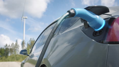 zoom out, graphics enhanced - a generic electric car charges in front of a wind turbine