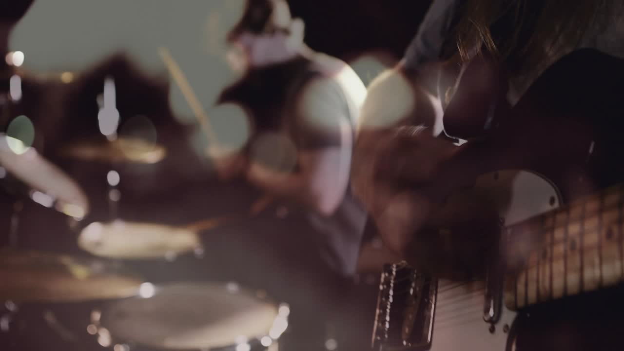 Chitarrista che suona il manico, chiamando il batterista, con bokeh che sovrappone gli strumenti, creando energia nella band.