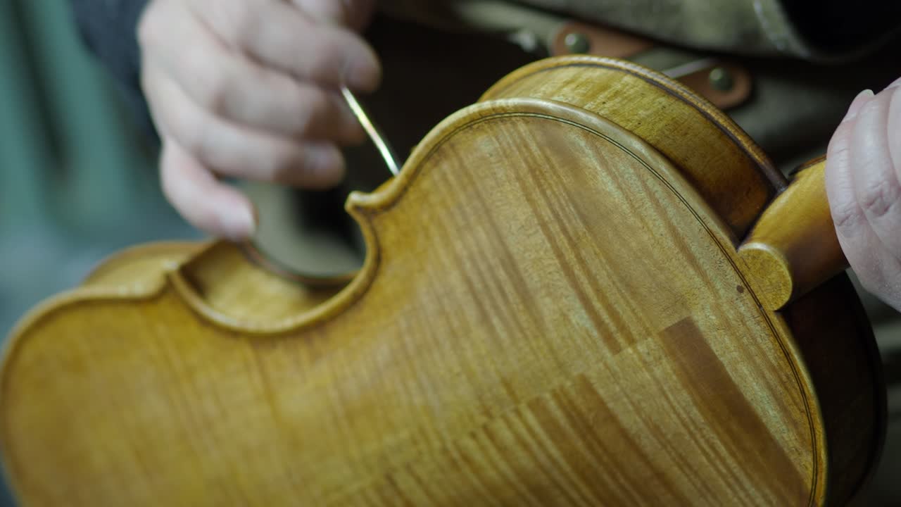 Close-up of a luthier applying varnish by hand to a finely crafted wooden violin in a traditional workshop