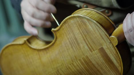 close-up of a luthier applying varnish by hand to a finely crafted wooden violin in a traditional workshop