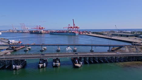 cars drive over fremantle traffic bridge with container cargo ships in background, perth, western australia