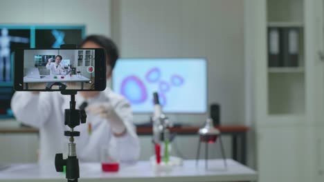 asian scientist man using smartphone recording video while researching in the laboratory, he holding test  tube and speaking