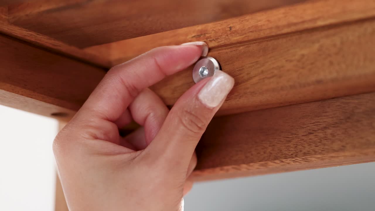 Close-up of a hand tightening a screw on wooden furniture. Bright lighting, steady camera, focused on precise assembly