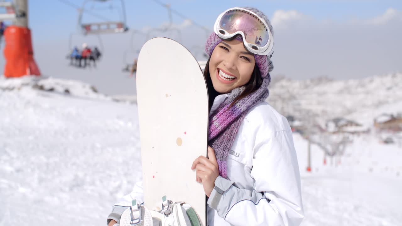 una mujer joven riendo con su snowboard.