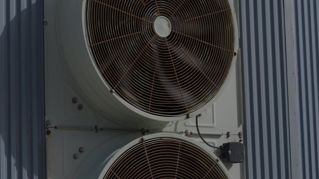 Large industrial exhaust fan with metal grill mounted on corrugated wall of factory exterior