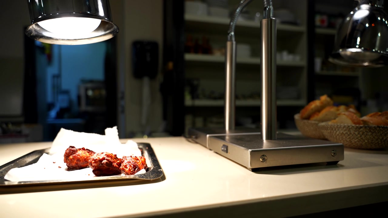 Chicken wings on a metal tray illuminated by a light bulb in a gloomy restaurant
