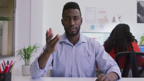 un hombre de negocios afroamericano sentado en un escritorio, haciendo una llamada de video en una oficina moderna.