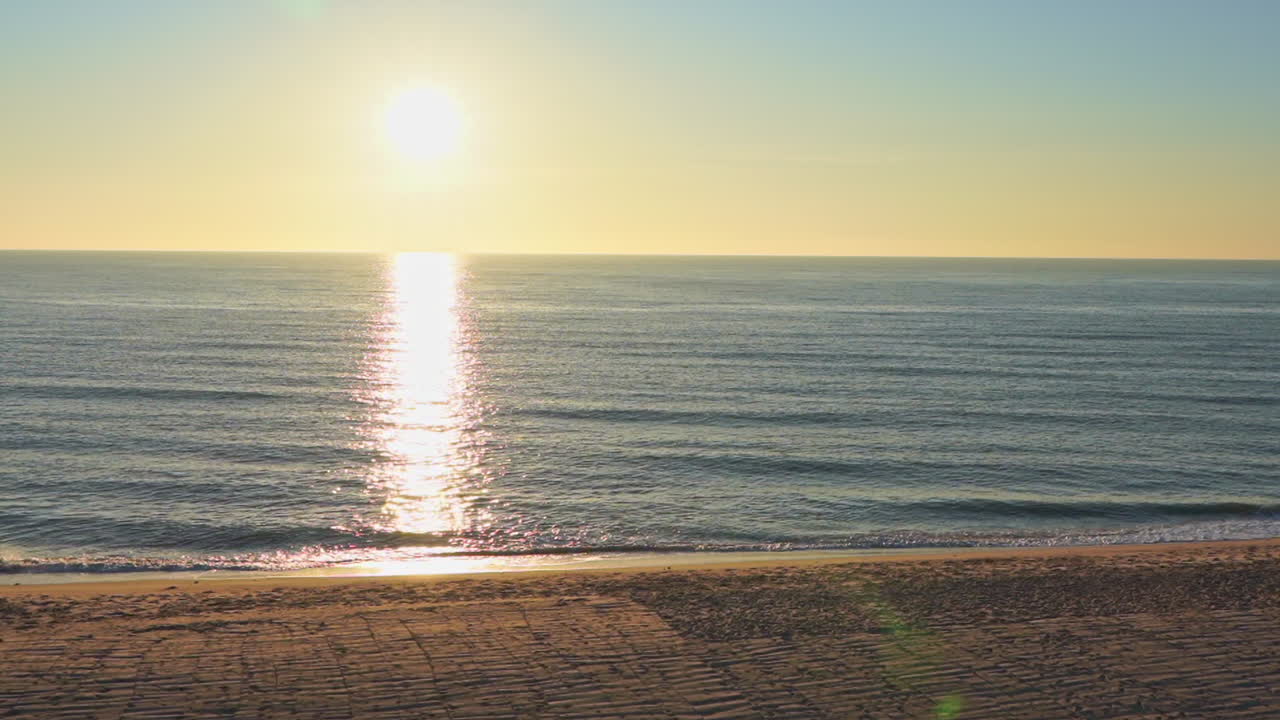 Golden seaside sunset sunrise at the beach. Small waves at low tide, sun reflections on the water