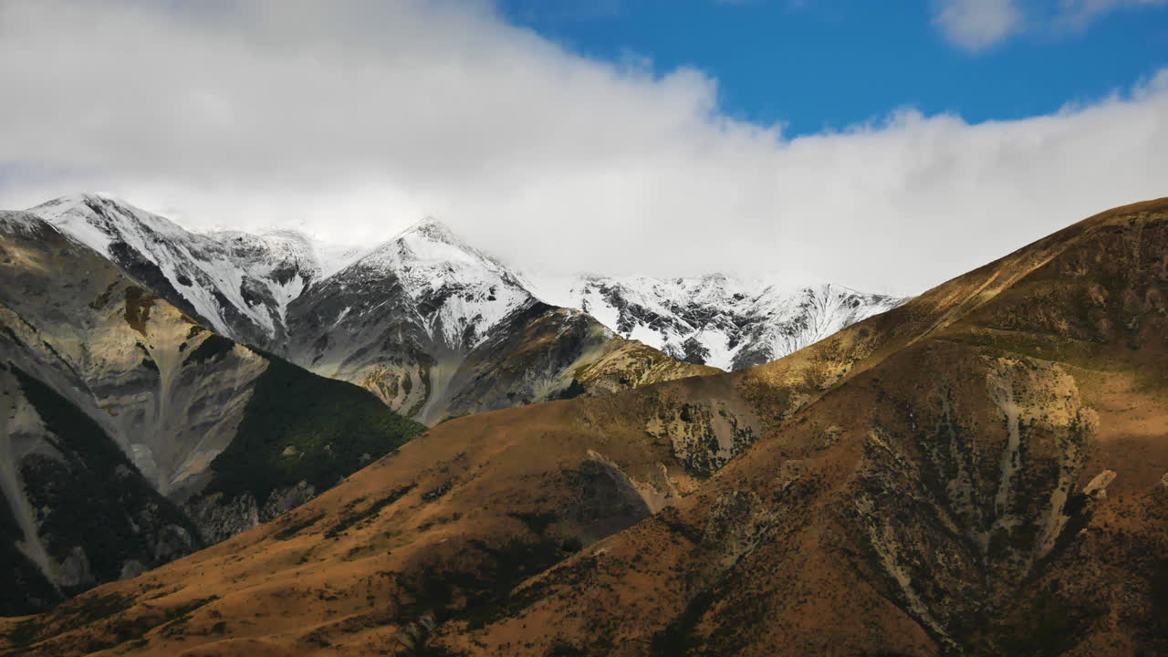 toma panorámica de cimas de montañas cubiertas de nieve y nubes blancas en el fondo en la colina del castillo, nueva zelanda