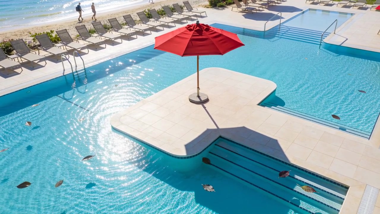 Framing red umbrella on beach pool deck, breeze rippling water, couple strolling in shorts