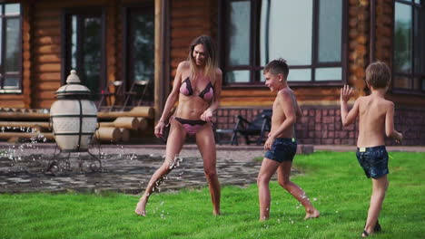 happy family with two kids playing with garden hose pouring water on grass