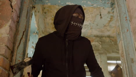 bottom view of a man in a black balaclava and holding an ax running in a ruined building