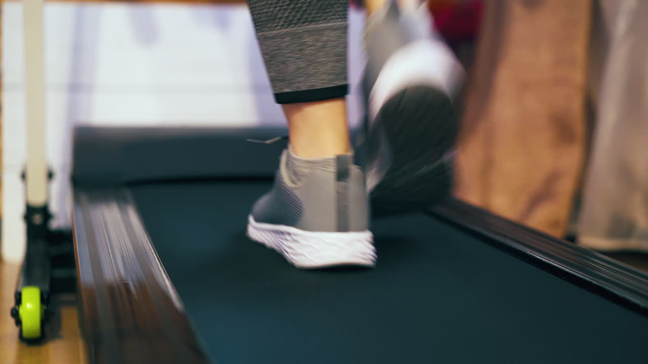 lady in sneakers walks along modern running machine in room