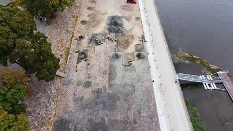 personas que trabajan en excavaciones arqueológicas junto al río, sobrevolando la vista
