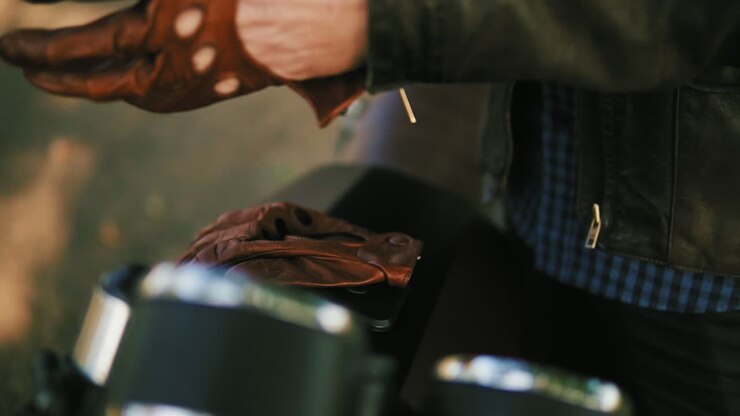 Unrecognizable motorcyclist coming up to his motorcycle, taking brown leather gloves and wearing special leather mitts for
