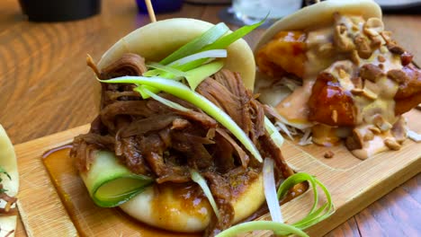 three delicious hot steam bao buns with pulled pork, coriander and crispy onions, duck and cucumber, fried chicken and peanuts, traditional asian food at a restaurant, 4k shot