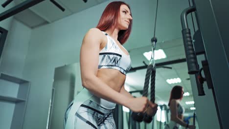close-up woman's body in sportswear training on a simulator. beautiful female with athletic body pulling rope on power training machine in modern fitness club.