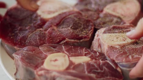 woman adding pepper to raw veal shank