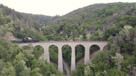 steam train passing over a stone viaduct in a mountain valley,zooming