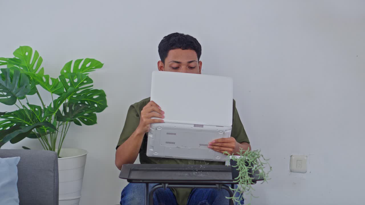Young man distracted by leaking roof while using laptop at home